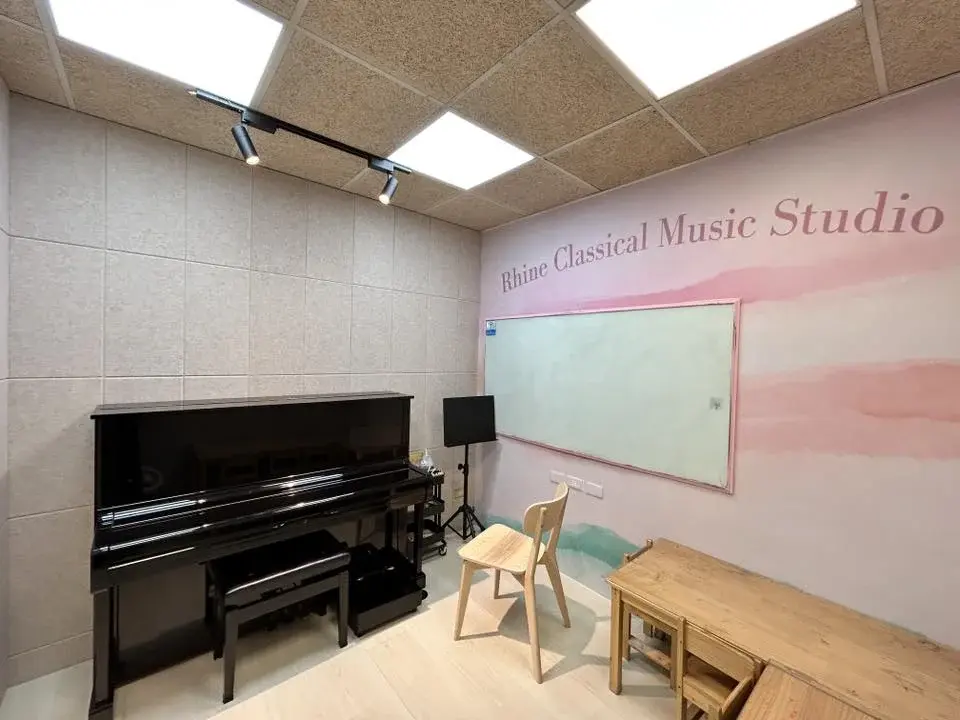 教室一角:直立鋼琴、原木桌椅、牆上 Rhine Classical Music Studio 題字